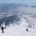 Skiers gracefully descend a snow-covered mountain at Schweitzer Mountain Resort, with frost-draped trees on either side. The sky is clear with some clouds, revealing distant peaks. The scene captures the vastness and beauty of a winter escape, perfect for those seeking Schweitzer vacation rentals.