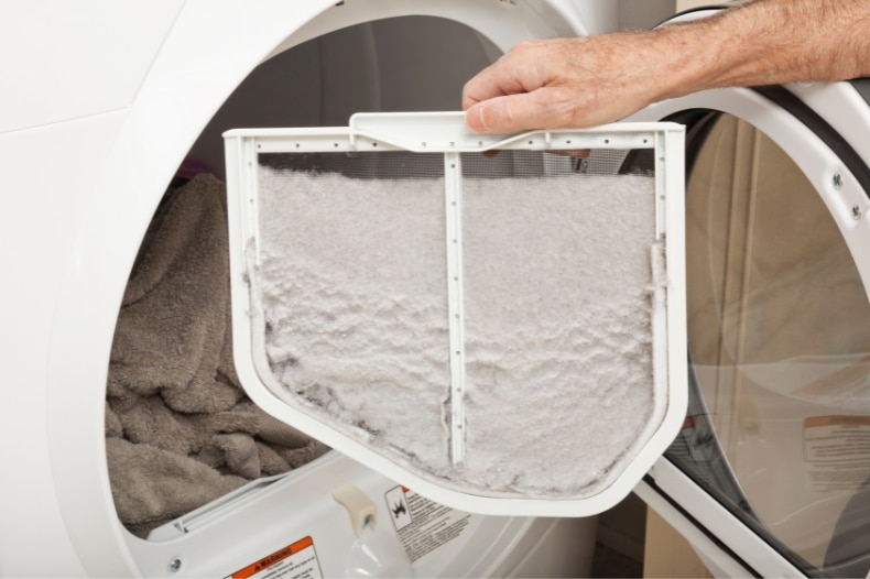 A hand pulls out a lint filter full of lint from a clothes dryer, with towels visible inside the drum—an essential STR maintenance tip for North Idaho property owners.