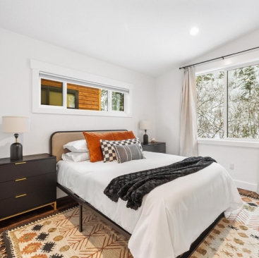 7 A modern bedroom with a neatly made bed, decorative pillows, black throw blanket, stylish nightstands and lamps, patterned rug, and large windows revealing snowy trees—perfect for a North Idaho Vacation Rental Management portfolio.