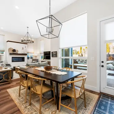4 A modern dining area with a dark wooden table, six chairs, a decorative rug, and geometric pendant lighting—perfect for entertaining. Large windows fill the space with light. Ideal for those seeking expert North Idaho Vacation Rental Management.