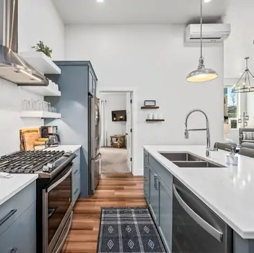 7 Modern kitchen with blue cabinets, stainless steel appliances, and a gas stove, perfect for enjoying your stay with North Idaho Vacation Rental Management. A doorway opens to a living room with a TV, enhancing this welcoming rental experience.