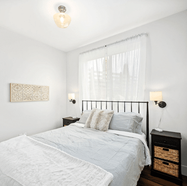 9 A bright bedroom with a large window, sheer white curtains, light gray bedding, black nightstands, and wall-mounted lamps—perfect for guests seeking comfort through North Idaho Vacation Rental Management.